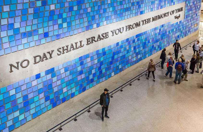 vista aérea de pessoas caminhando em uma das salas do museu 11 de setembro, onde há a frase ''no day shall erase you from the memory of time'' na parede
