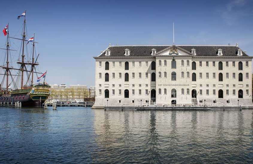 durante o dia, grande prédio branco em às margens de rio, onde funciona um dos museus em amsterdam