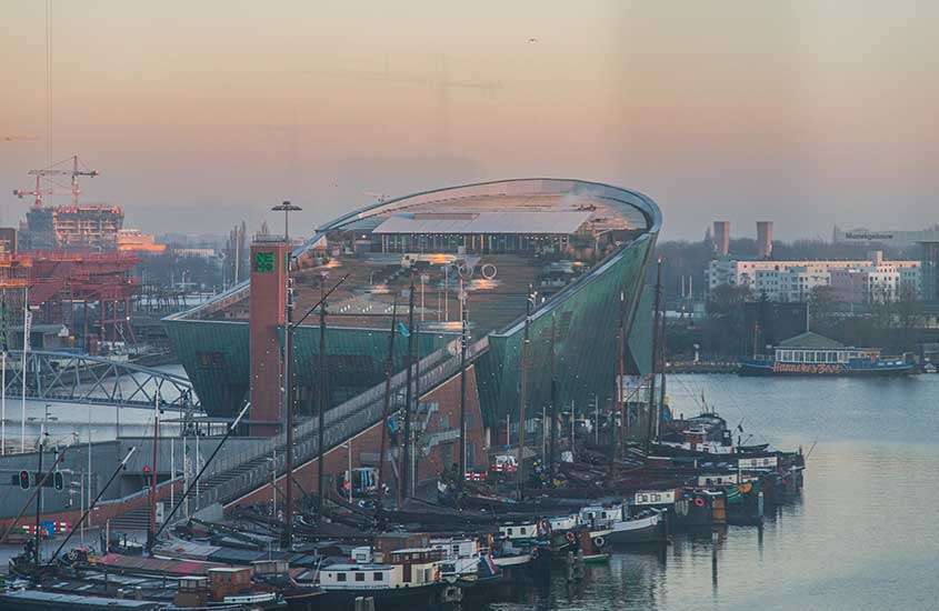 durante entardecer, vista aérea de prédio em forma de navio, às margens de rio em Amsterdam