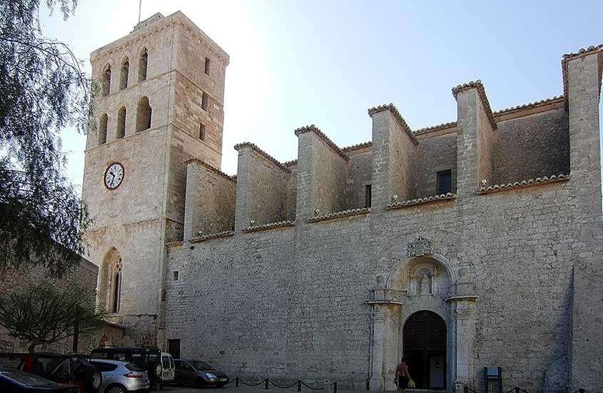 Durante o dia, carros estacionados em frente à catedral em Ibiza com arquitetura gótica catalã.
