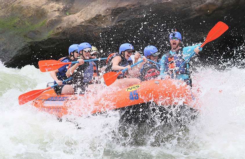 durante o dia, diversas pessoas em bote laranja, se divertindo em rafting no rio Mendoza.