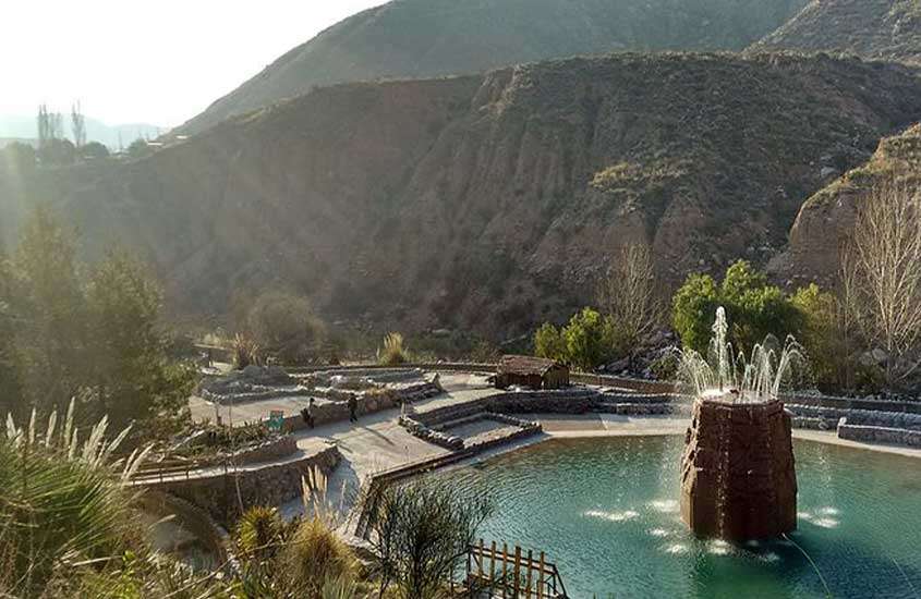 durante um dia ensolarado, vista aérea de árvores e montanhas ao redor de piscina em termas Cacheuta, um dos pontos turísticos de mendoza.