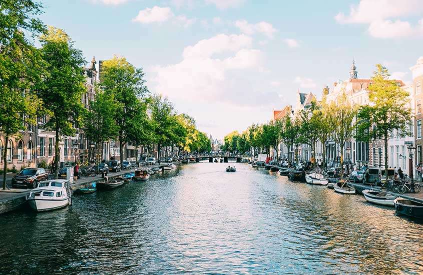 Durante dia ensolarado, vista panorâmica de barcos em canal de Amsterdam, um lugar para quem busca o que fazer na Holanda