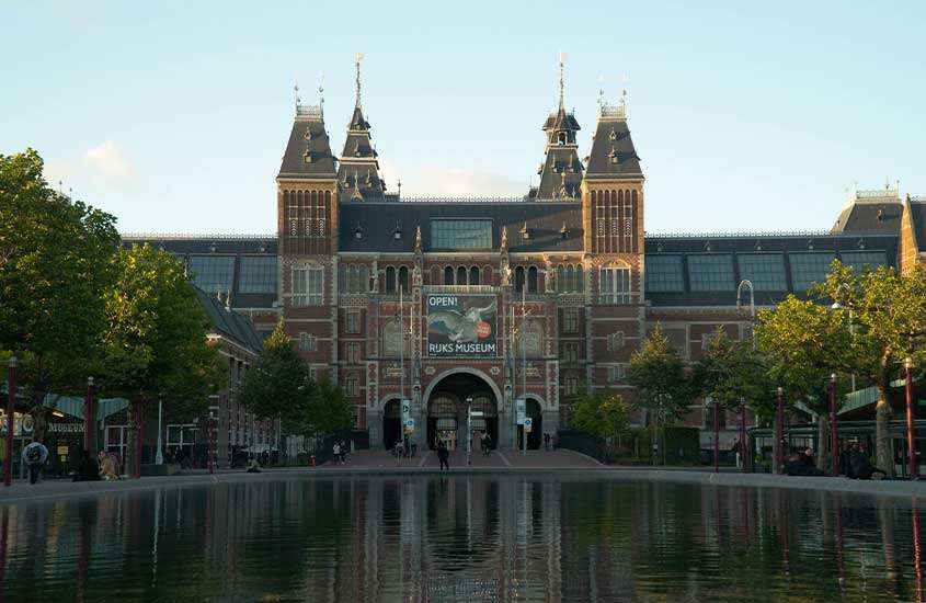 durante o dia, lago e árvores em frente a fachada do Rijksmuseum, um dos pontos turísticos da holanda