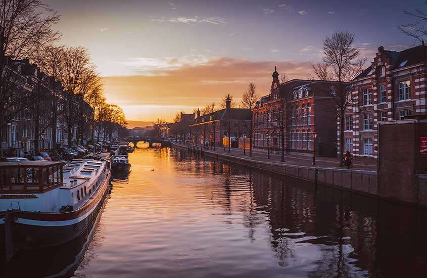 Durante um entardecer, vista panorâmica de barcos em canal de amsterdam, uma das cidades da holanda para conhecer