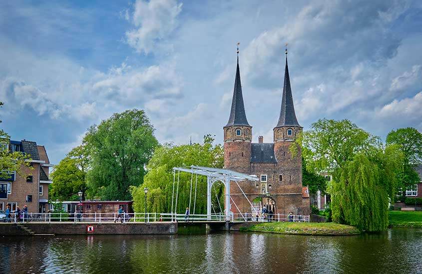Durante o dia, vista panorâmica de árvores e prédios às margens de lago em Delft um dos principais pontos turísticos da holanda