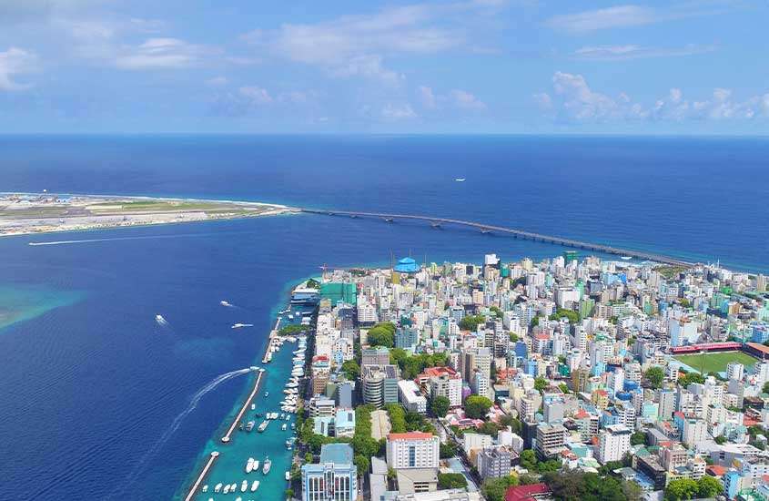 Vista aérea durante o dia de prédios localizados às margens do mar em Malé, a capital das Maldivas, mostrando a mistura entre a arquitetura urbana e a beleza natural do entorno marítimo.