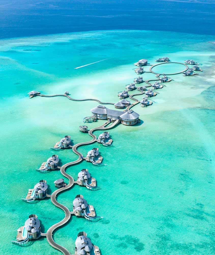 Durante um dia ensolarado, vista aérea de diversos bangalôs sobre as águas cristalinas de uma das ilhas das Maldivas.