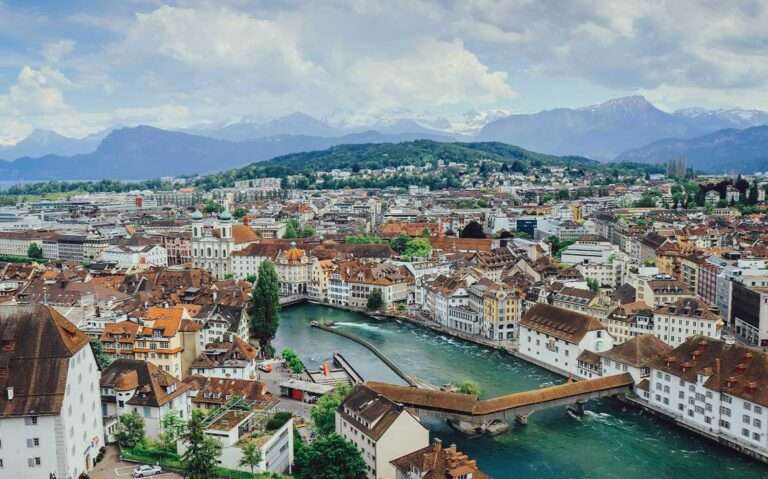 Durante o dia, vista aérea de diversas casas e montanhas às margens de rio em Lucerna.