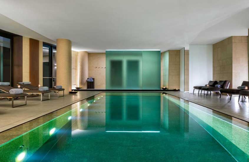 diversas espreguiçadeiras em frente a grande piscina retangular em área de lazer coberta de um dos melhores hotéis em Milão.