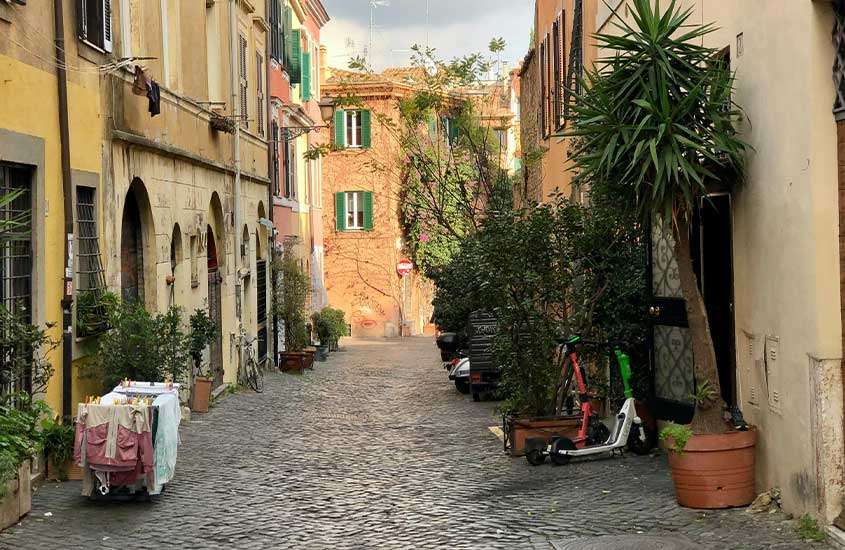 Ruela com prédios coloridos, patinetes, varal estendido com roupas e vasos de plantas em Trastevere, um lugar onde ficar em Roma.