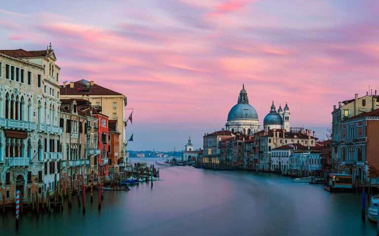 Vista panorâmica durante o entardecer de casas coloridas alinhadas às margens de um dos canais em Veneza, criando uma cena encantadora e pitoresca.
