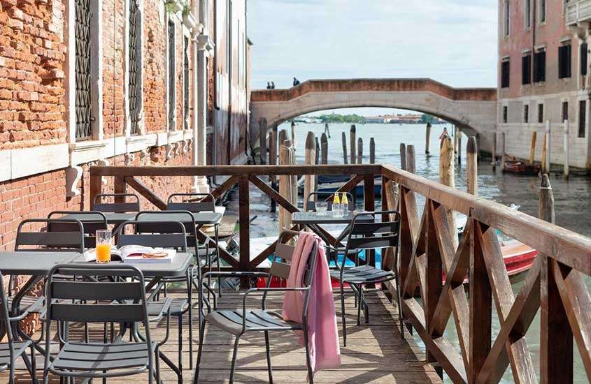 Durante o dia, mesas e cadeiras em deck de hotel em Veneza com vista para os canais.