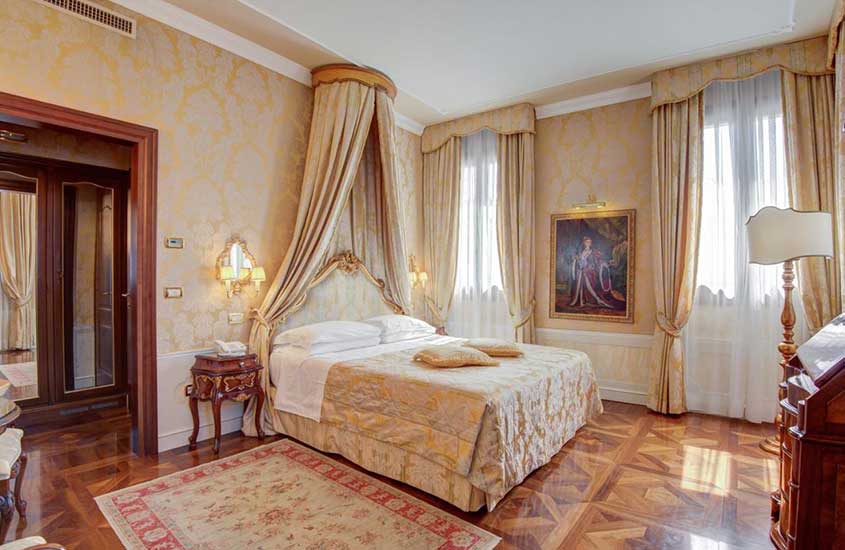 Quarto de um dos hotéis em Veneza próximo a estação de trem, equipado com cama de casal, espelho e quadros de arte.