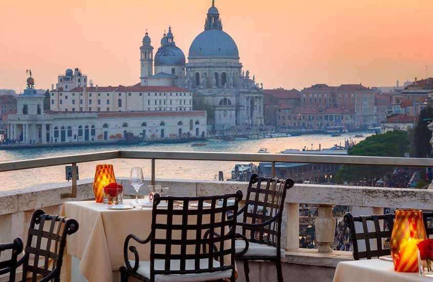 Durante o entardecer, mesas de jantar em terraço de hotel em Veneza com vista para o Grande Canal.
