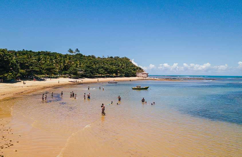 Vista panorâmica, durante o dia, de pessoas tomando banho em mar calmo e raso de Caraíva, uma das praias mais bonitas do nordeste do Brasil.