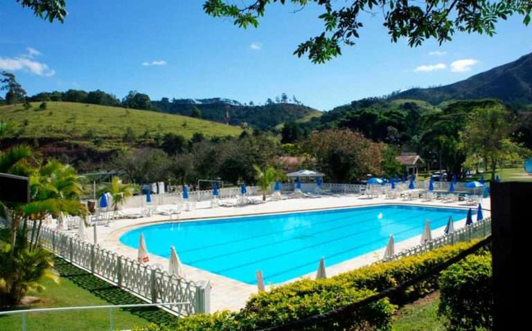 Durante um dia ensolarado, espreguiçadeiras ao redor de grande piscina externa de um dos melhores hotéis em Águas de Lindóia com vista para as montanhas