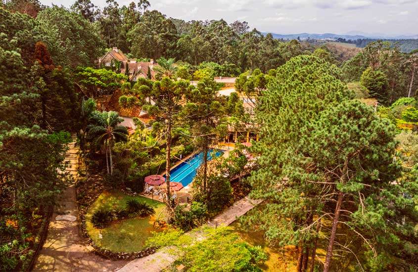Durante o dia, vista aérea de piscina ao ar livre rodeada por árvores em hotel fazenda no interior de São Paulo