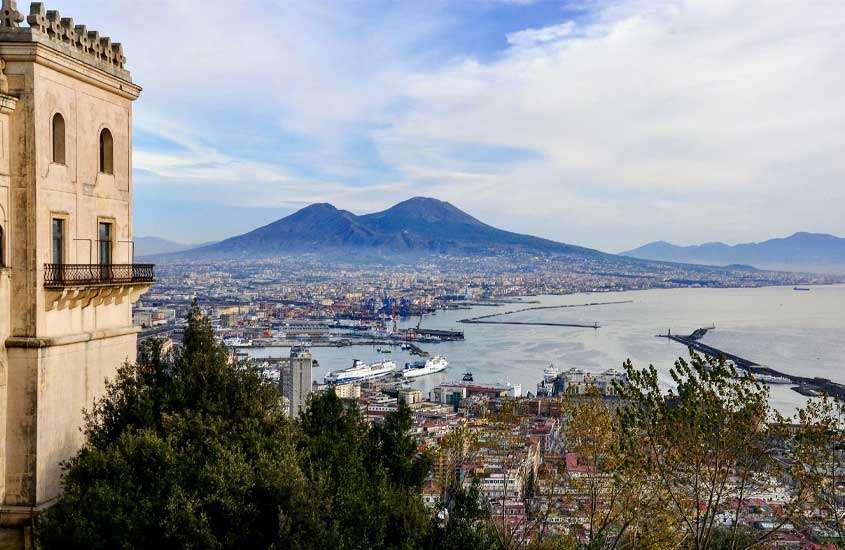 Visão aérea da paisagem da cidade de Nápoles com casas, árvores, mar e, ao fundo, montanhas