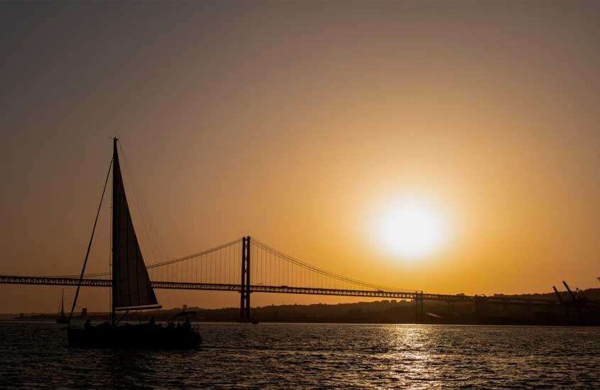 Durante o pôr do sol, vista do rio Tejo com barco á esquerda e ponte Vasco da Gama ao fundo