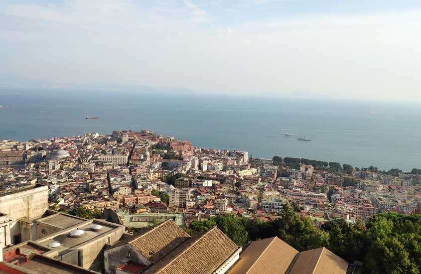 Durante o dia, visão aérea de casas, árvores e mar em Vomero, um lugar onde ficar em Nápoles
