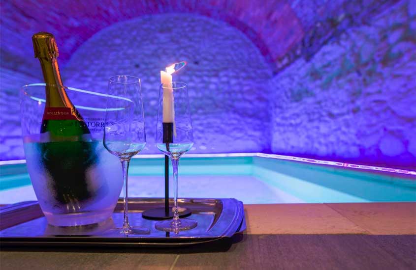 bandeja de champagne, taças e vela em borda de piscina externa com iluminação azul e parede de tijolos