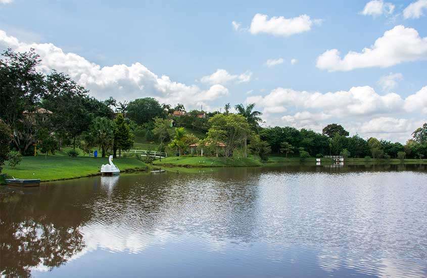 Em tarde de clima ameno, lago com pedalinho, rodeado por árvores