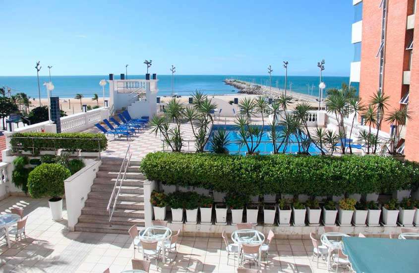 Em dia ensolarado, vista aérea de piscina, espreguiçadeiras, mesas e cadeiras em área de lazer de um dos hotéis em fortaleza beira mar