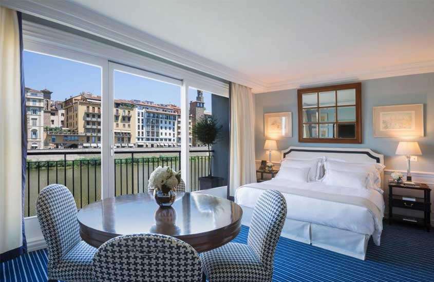 Durante o dia, quarto de hotel em Florença, mobilhado com mesa decorada com flores, luminária e espelho, cadeiras e vista da cidade