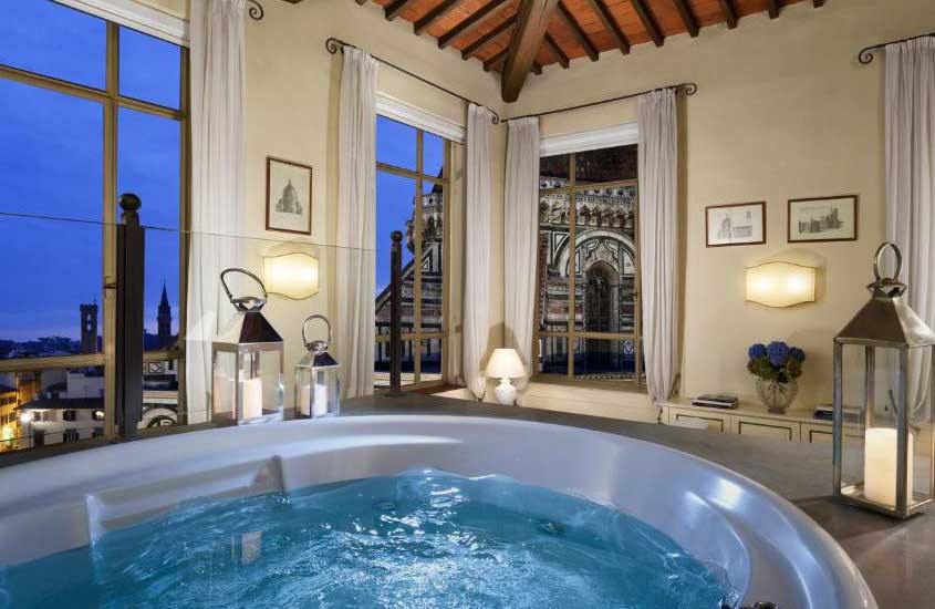Durante o anoitecer, quarto de hotel em Florença mobilhado com banheira de hidromassagem e grandes janelas com vista para a cidade