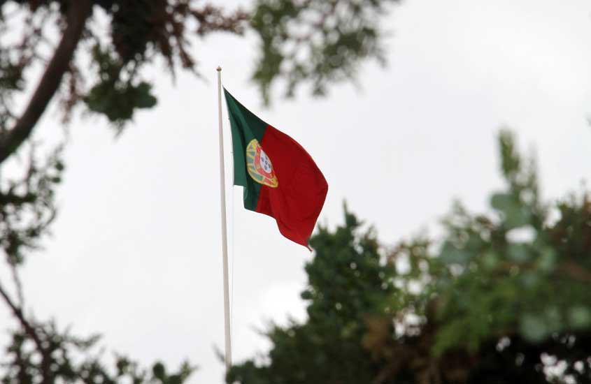 Durante tarde nublada, bandeira de Portugal hasteada com árvores atrás