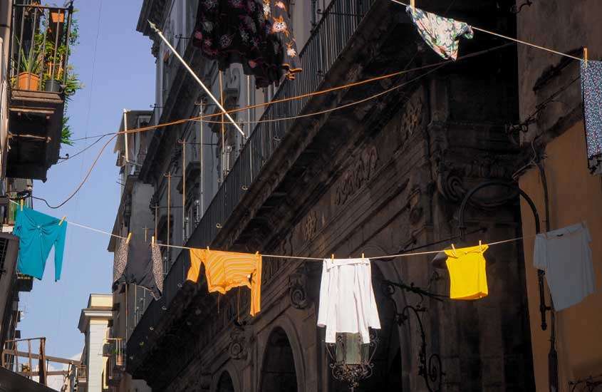 Durante o dia, varal de roupas pendurado entre prédios em rua de Nápoles