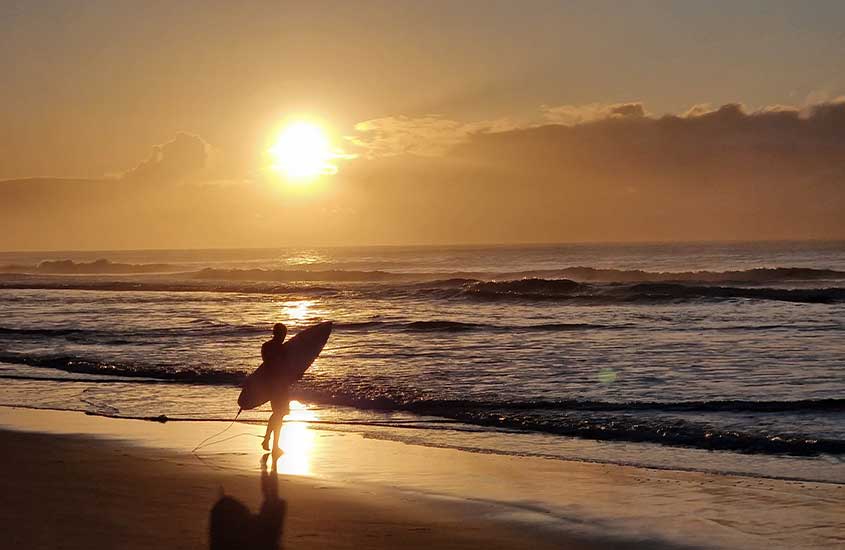 Em dia ensolarado, surfista indo em direção ao mar de Porto de galinhas, uma das cidades bonitas do Brasil.