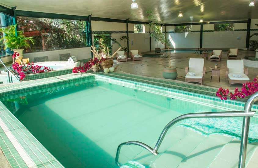 Piscina aquecida interna de hotel em aguas de lindoia com área de spa e espreguiçadeiras brancas