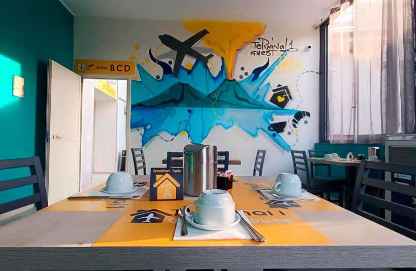 Sala de café da manhã com mesas postas e pintura de aviões na parede