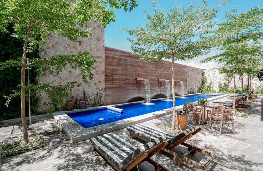 Em dia de sol, piscina externa com espreguiçadeiras de madeira, cascatas e árvores em volta em um dos hotéis beira mar em fortaleza