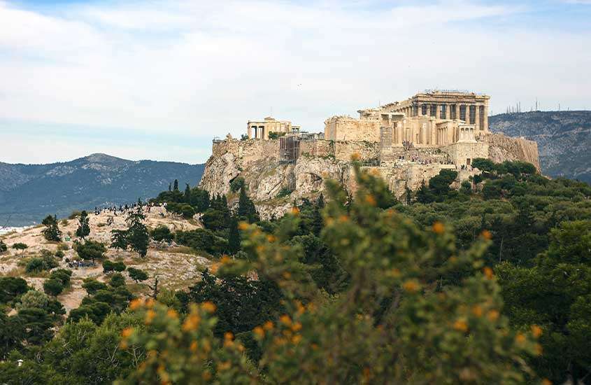 Em dia de sol, vista panorâmica da acrópole de Atenas com montanhas e árvores em volta