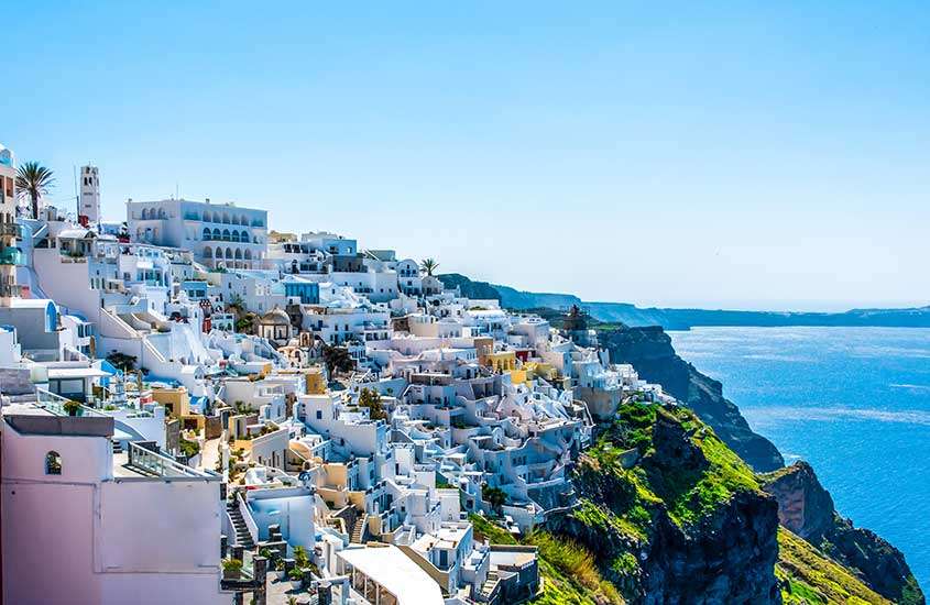 Em dia de sol, casas em montanha às margens do mar em um dos pontos turísticos da Grécia