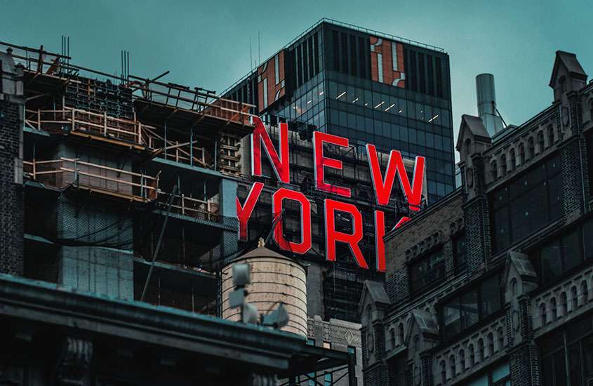 ao anoitecer, construção inacabada com letreiro vermelho escrito “New York” e prédios em volta