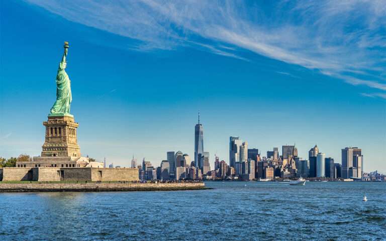 durante o dia, vista panorâmica da cidade de nova york com estátua da liberdade a esquerda, e prédios ao fundo