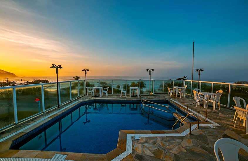 Durante um pôr do sol, mesas, cadeiras guarda e piscina em cobertura de hotel em ubatuba com vista para o mar