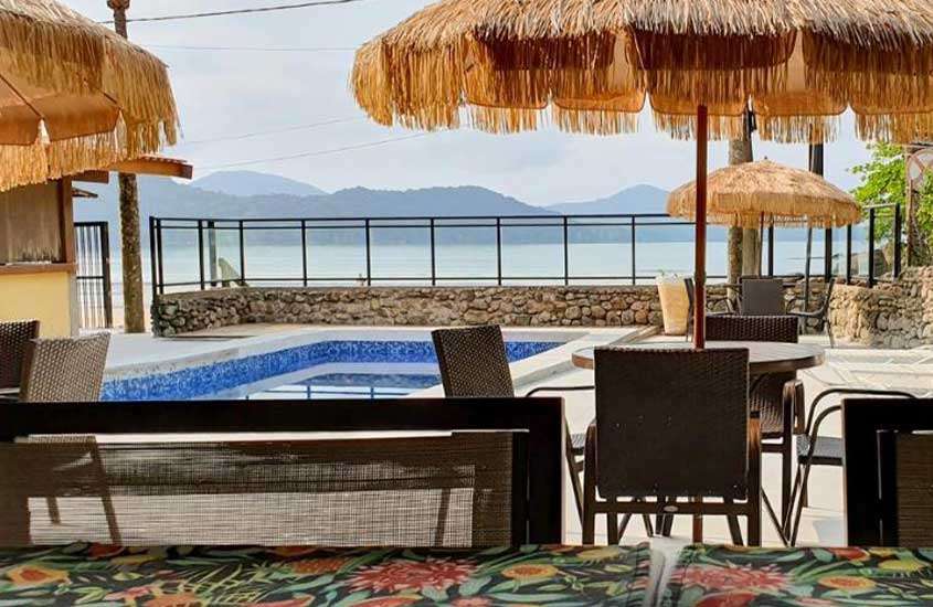 em manhã de céu azul claro, mesas e cadeiras ao redor de piscina em área de lazer de um dos melhores pousadas pé na areia em ubatuba