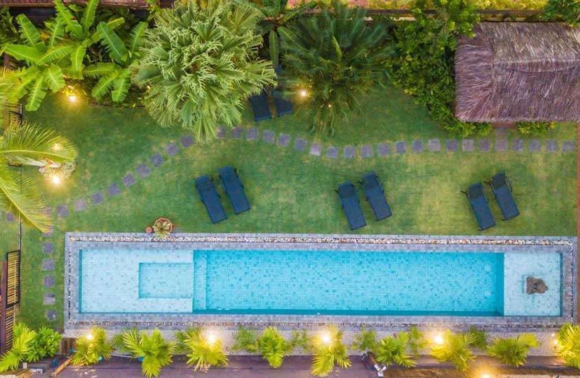 Vista aérea de árvores e espreguiçadeiras ao redor de piscina ao ar livre em área de lazer de hotel