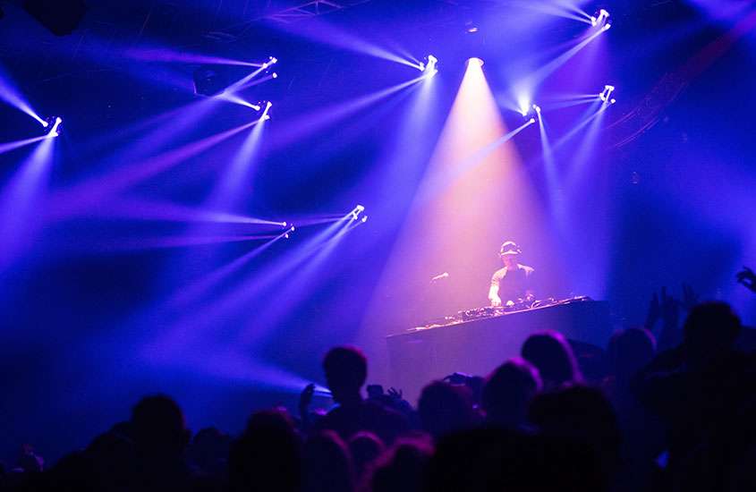 Pessoas dançando em frente a mesa de DJ em boate com luzes roxas, durante festa de ano novo em buenos aires