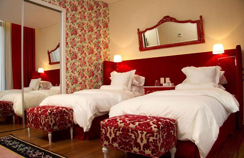Quarto decorado em branco e vermelho com duas camas de solteiro, tapete e espelho
