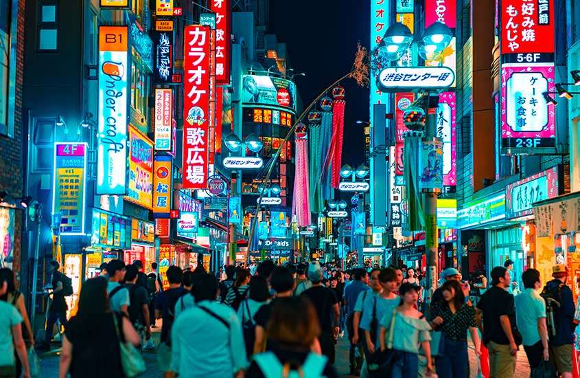 Durante a noite, rua movimentada, com várias pessoas caminhando prédios com painéis luminosos em Tokyo, lugar para incluir roteiro japão