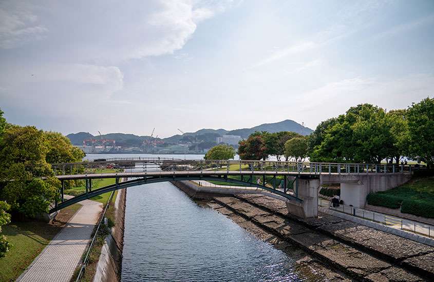 Durante um dia de sol, vista aérea de árvores ao redor de ponte sobre o rio, em Nagasaki, uma das cidades para visitar no Japão