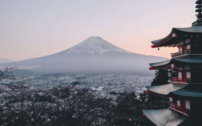 Vista aérea panorâmica de construção vermelha ao lado direito, diversas construções e monte Fuji ao fundo