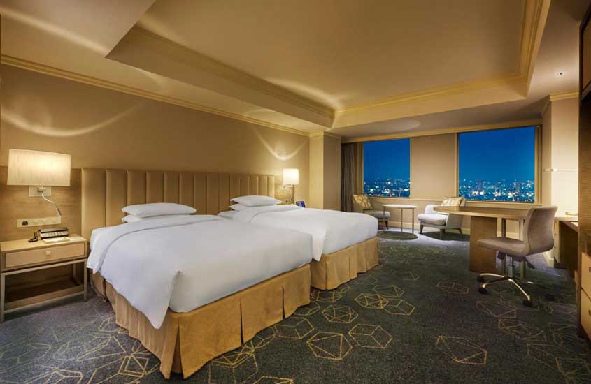 Durante a noite, duas camas de casal, área de trabalho, mesa com cadeiras e janelas grandes com vista da cidade em hotel em Nagoya