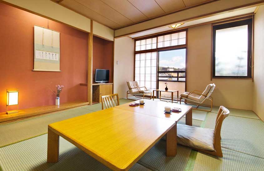 Durante o dia, acomodação de hotel em Takayama com mesas, cadeiras, televisão e janelas grandes com vista para a cidade
